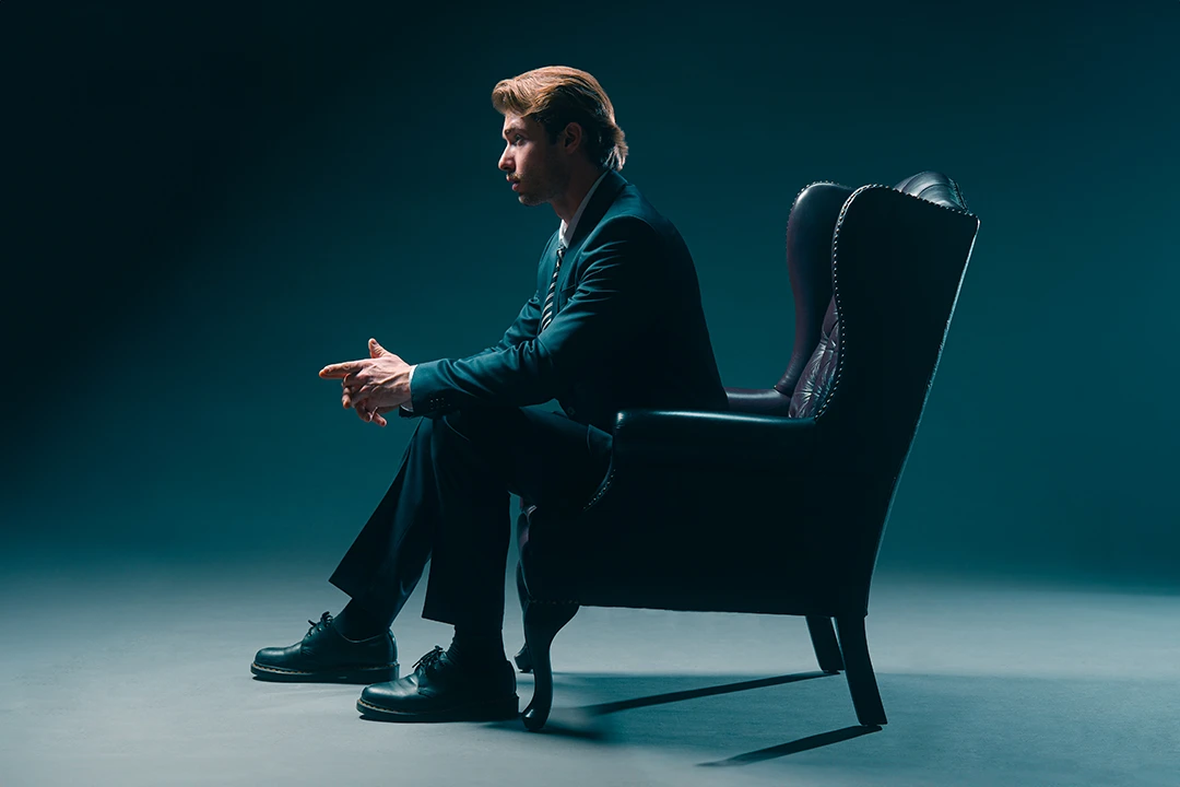 fashion portrait of man sitting in wingback chair in a photo studio